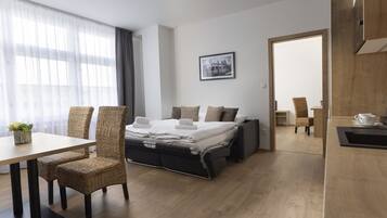 Une chambre d’hôtel moderne, équipée d’un lit, de deux fauteuils en osier, d’une table à manger et d’une petite table d’appoint sur laquelle se trouve une tasse.