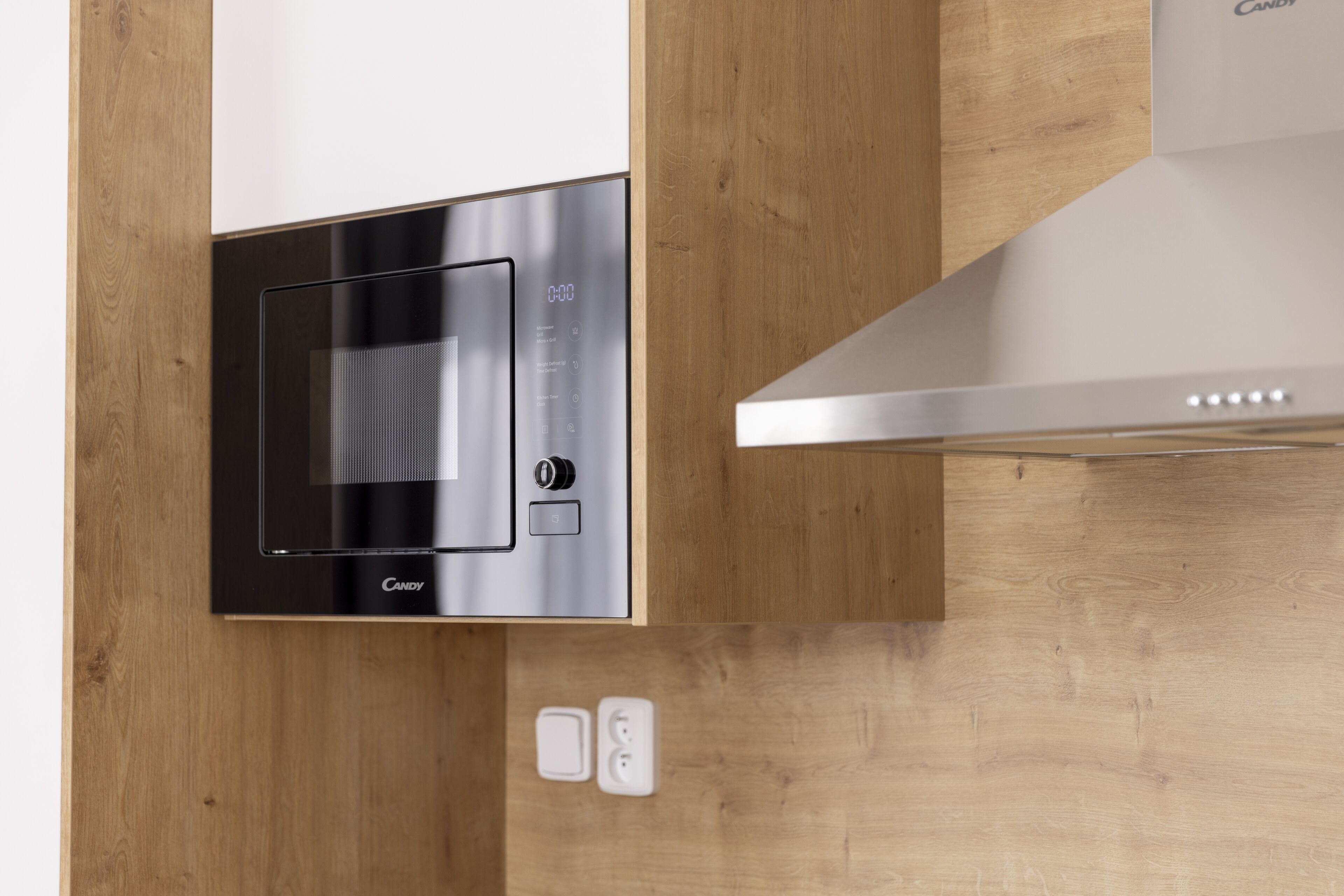 Uma cozinha moderna com micro-ondas integrado, exaustor de aço inoxidável e bancada de madeira.