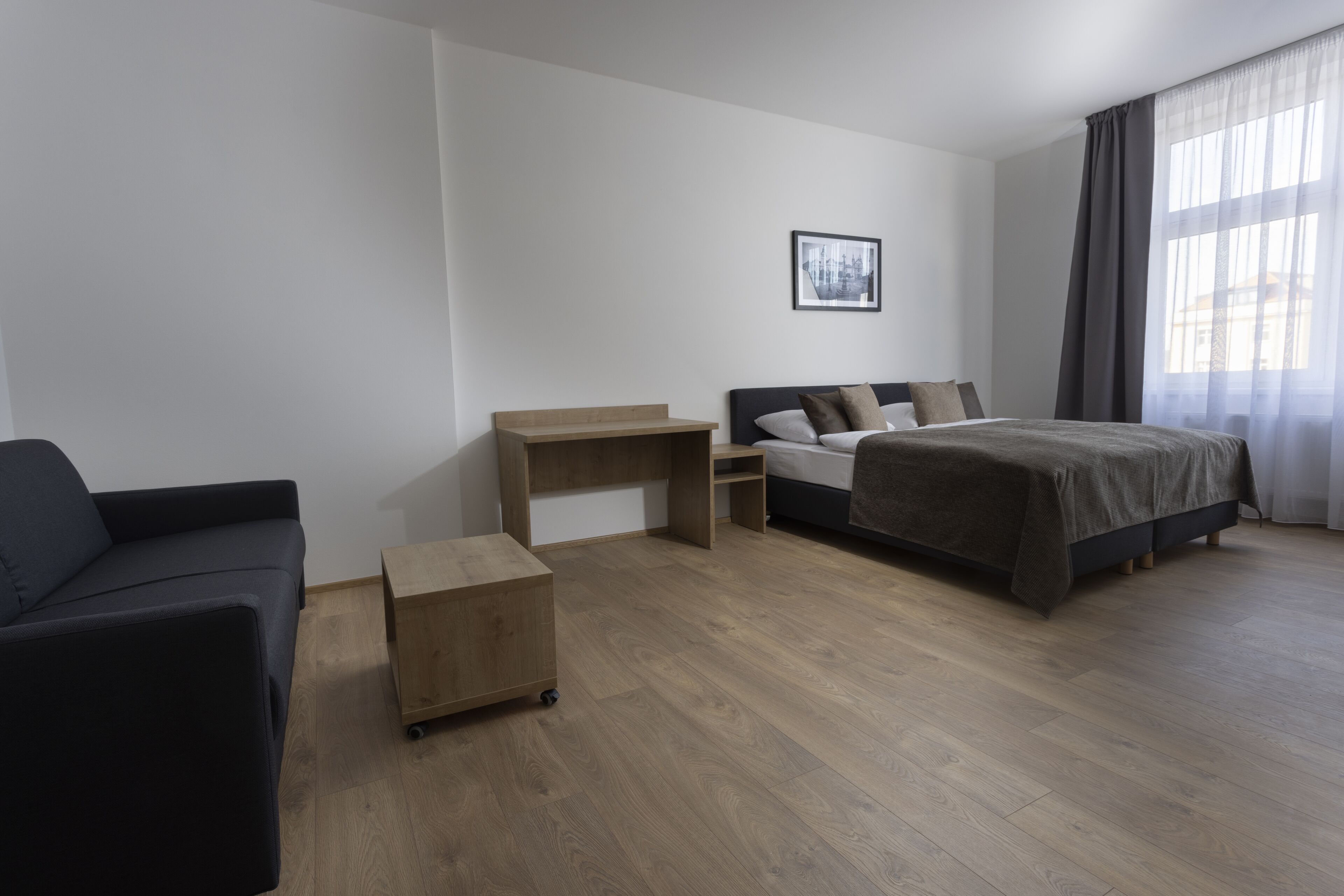 Ein modernes Hotelzimmer mit einem Bett, einem Schreibtisch, einer Couch und einem kleinen Holzschrank.
