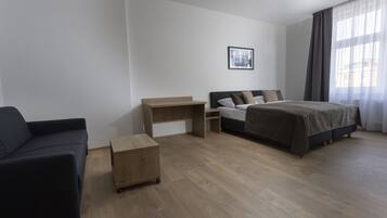 Ein modernes Hotelzimmer mit einem Bett, einem Schreibtisch, einer Couch und einem kleinen Holzschrank.