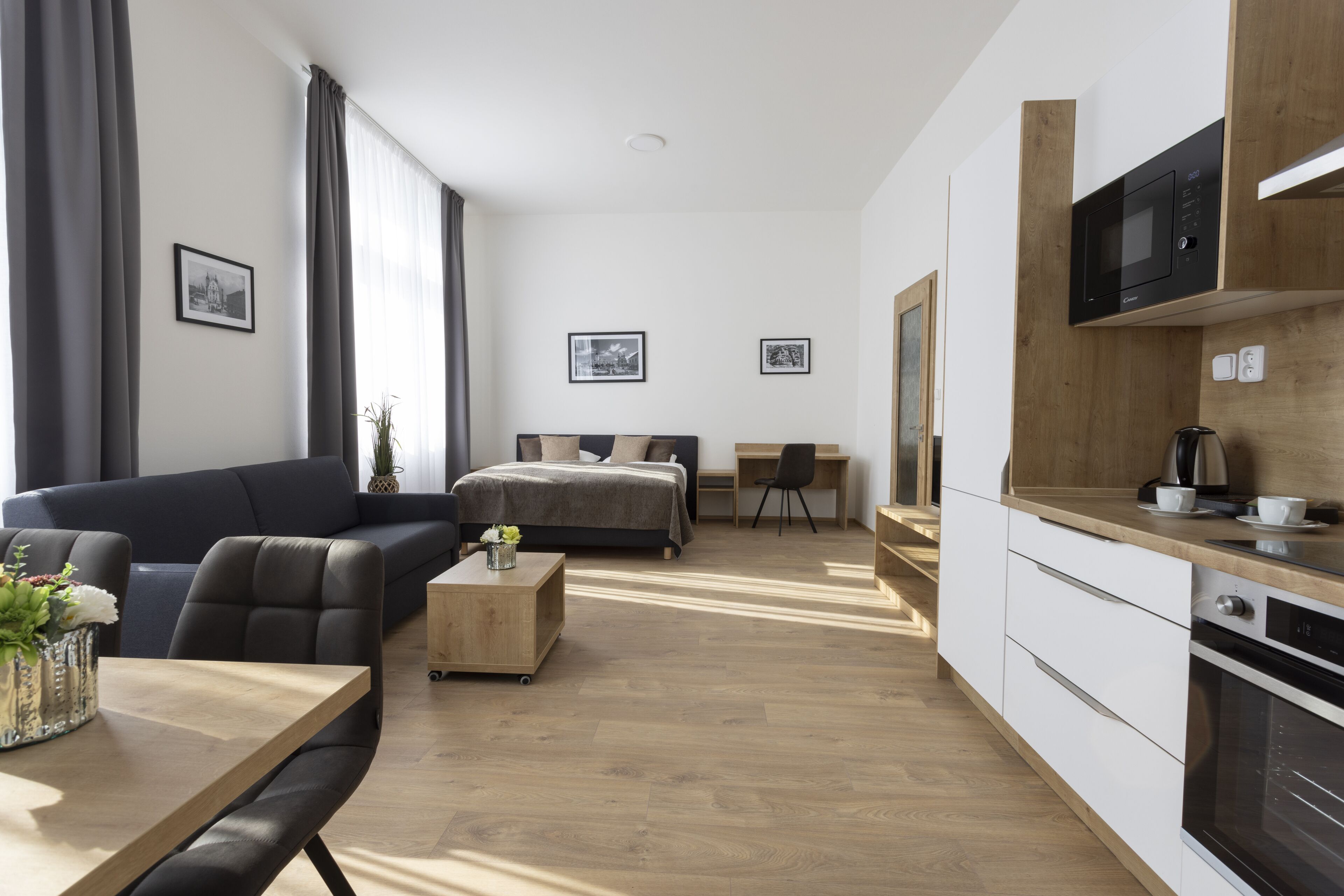 A modern hotel room with a sofa, a bed, a desk, and a kitchenette.