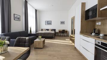 A modern hotel room with a sofa, a bed, a desk, and a kitchenette.