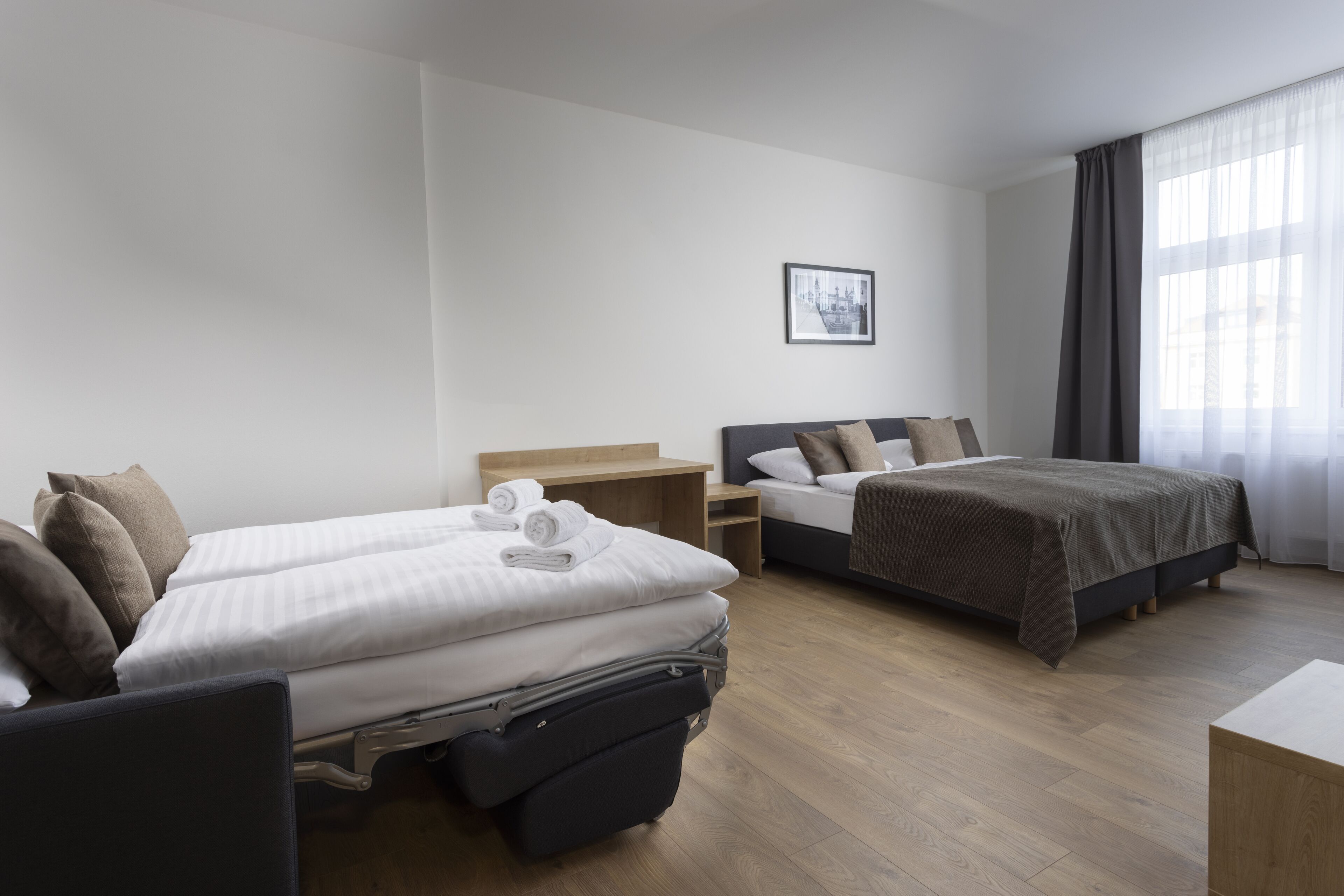Ein Hotelzimmer mit zwei Betten, einem Schreibtisch und einem großen Fenster mit Vorhängen.