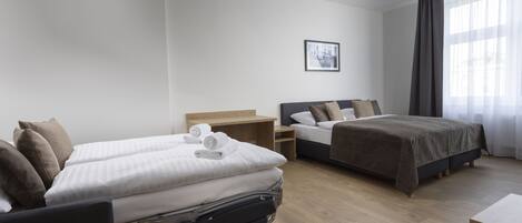 Una habitación de hotel con dos camas, un escritorio y un ventanal grande con cortinas.