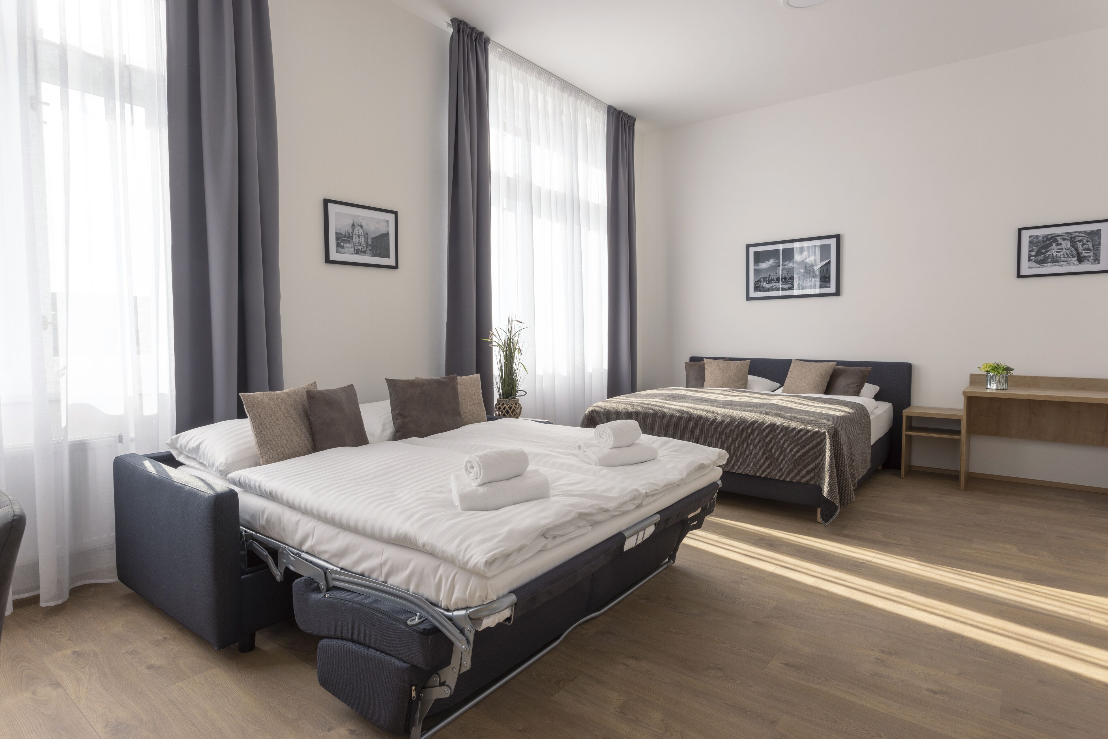 Moderni hotellihuone, jossa on kaksi sänkyä, työpöytä ja suuri ikkuna, jossa on verhot.