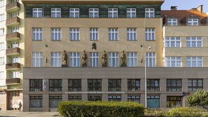 Un edifici de diversos pisos amb una entrada central, grans finestres i un terrat pla.
