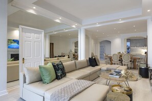 A spacious living room with a large beige sofa, a glass coffee table, and a dining area with a wooden table and chairs.
