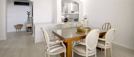 Un comedor con una mesa de madera y seis sillas, una cocina al fondo y una mesita con una planta.
