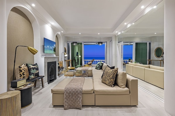 A spacious living room with a large beige sofa, a fireplace, and a view of the ocean.