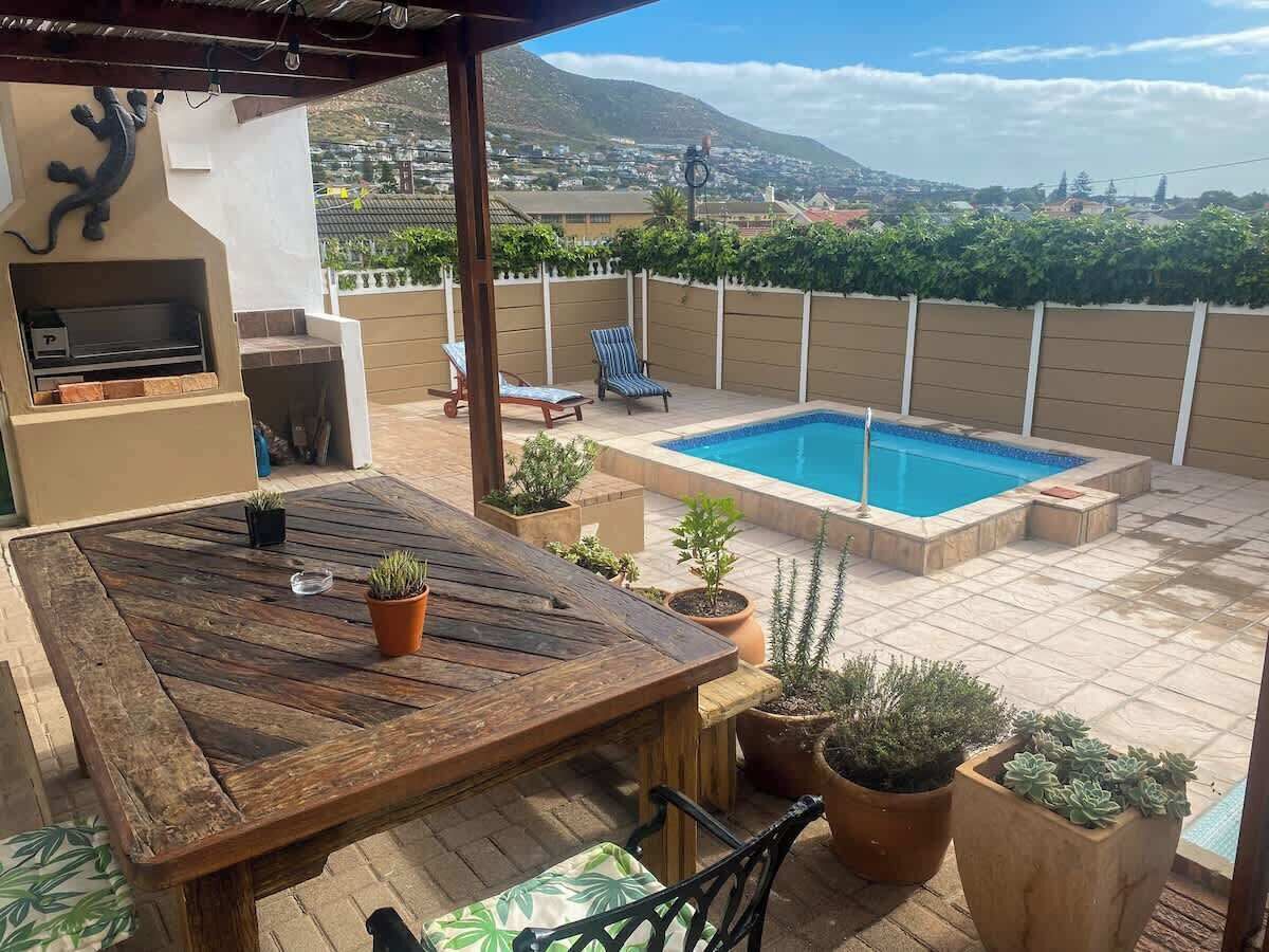 Eine Terrasse mit Holztisch, Blumentöpfen, einem Pool und Blick auf eine gebirgige Landschaft.