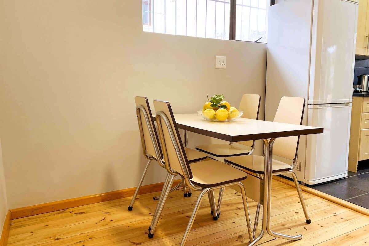 A kitchen with a white refrigerator, a wooden table with chairs, and a bowl of lemons on the table.