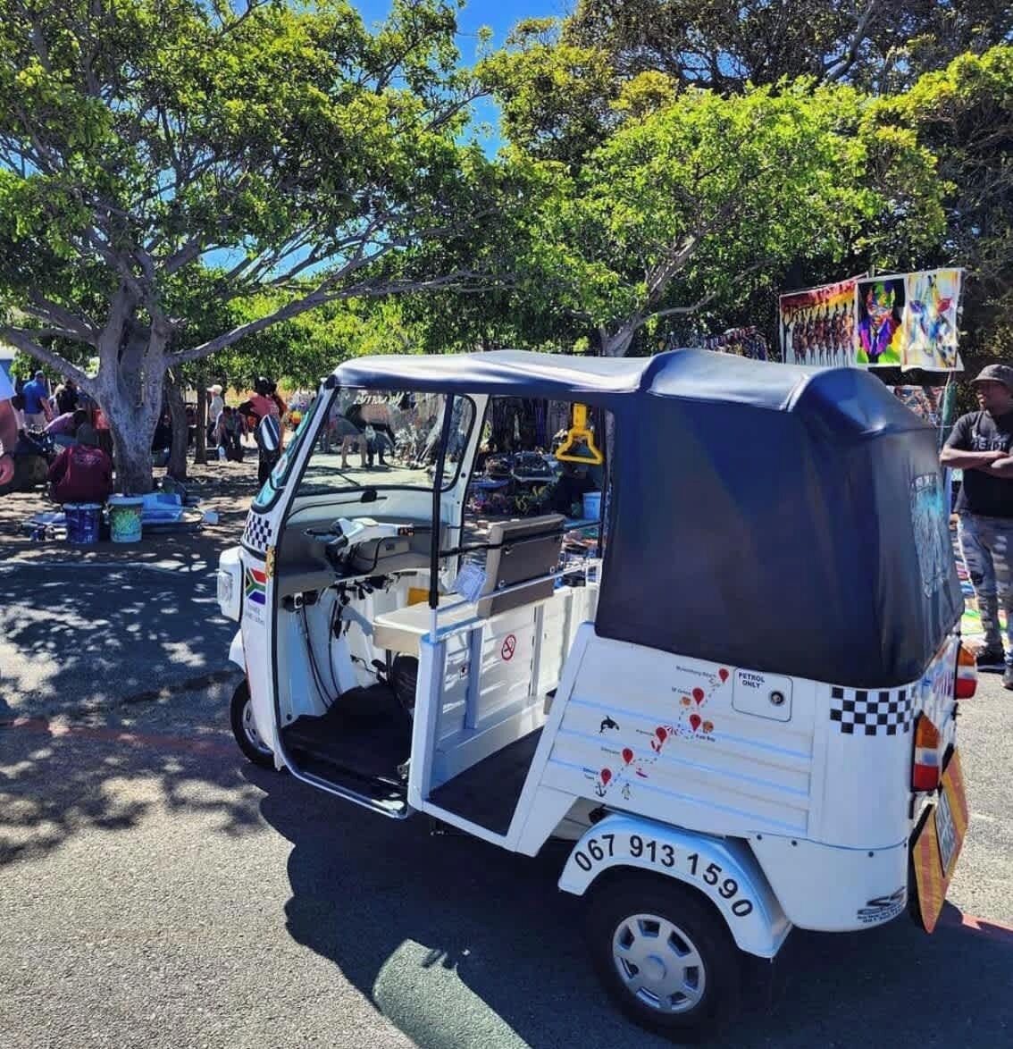 Un tuk-tuk bianco parcheggiato in una zona riparata, con alberi sullo sfondo.