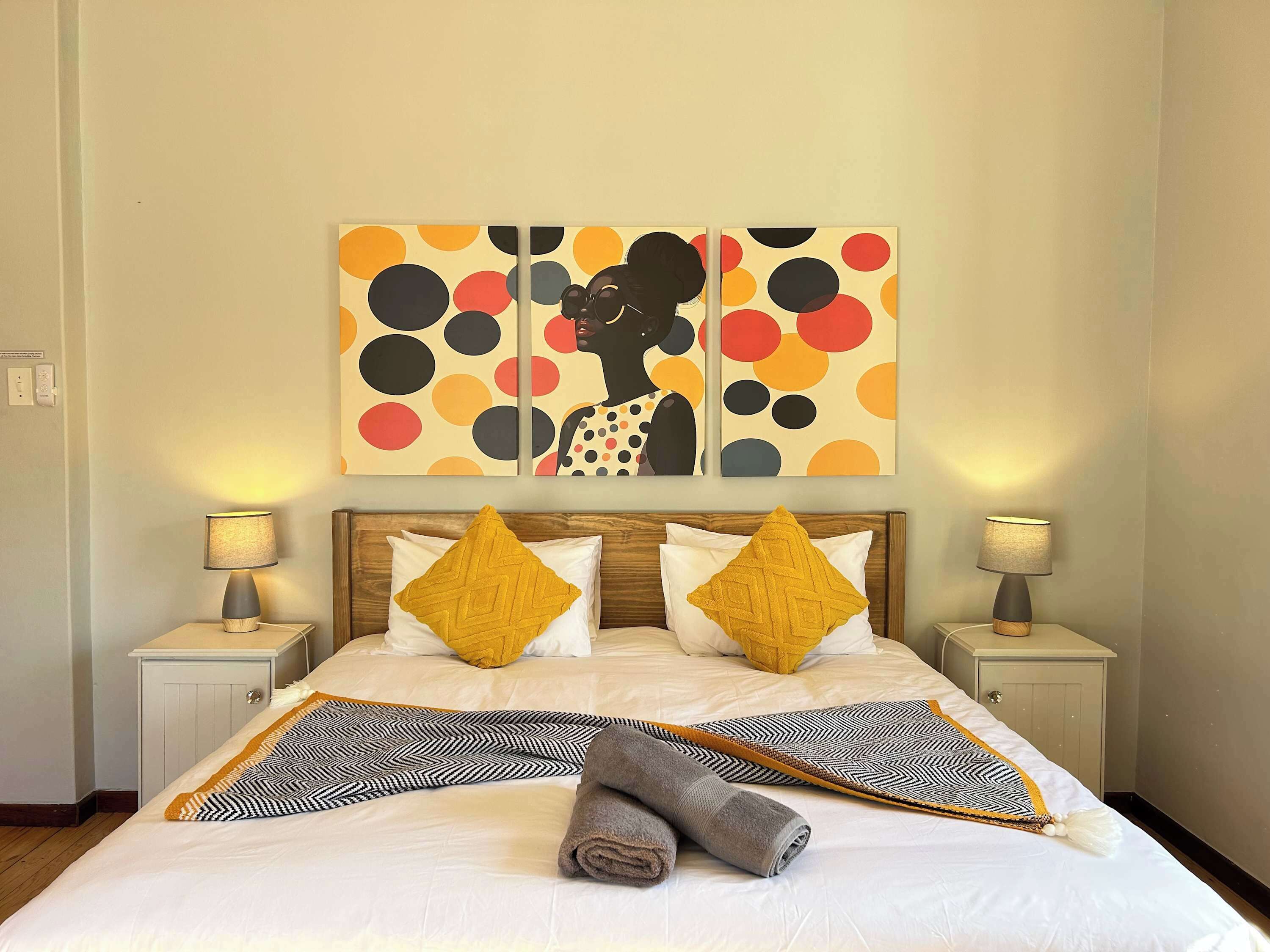 A neatly made bed with two pillows, a patterned throw, and rolled towels.