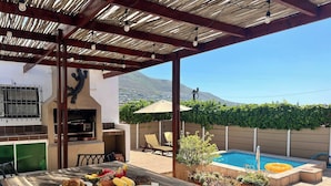 An outdoor patio with a wooden table set for a meal, a barbecue grill, and a swimming pool in the background. - Fuss-Free Family home | Pool & Fireplace (Cape Town)