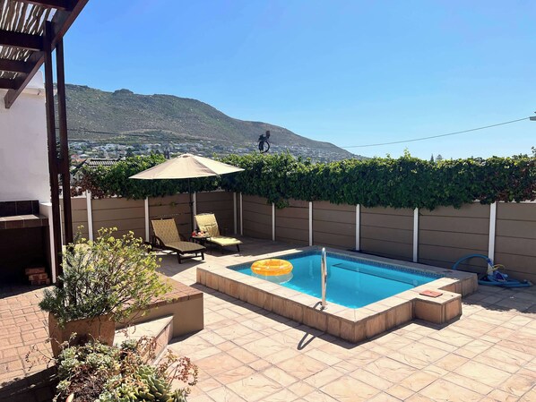 A backyard with a swimming pool, two lounge chairs, a potted plant, and a view of a mountain.