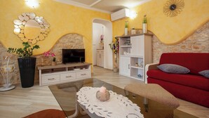 A living room with a stone fireplace, a TV on a wooden stand, a red sofa, and a white cabinet. - Pokrajac in Rovinjsko Selo  - Haus für 4-5 Personen (Rovinj)