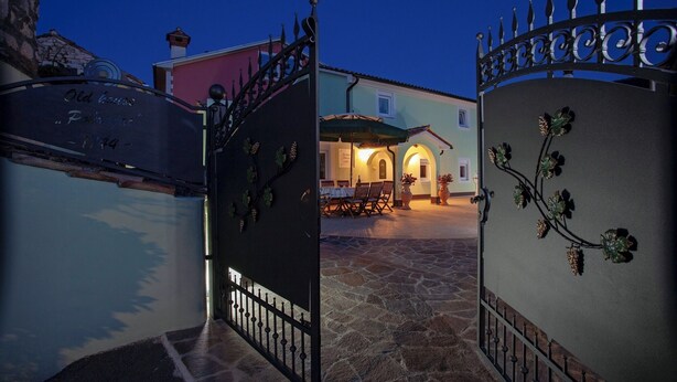 A stone-paved courtyard with a dining area, a gate with a vine decoration, and a building with a pink facade. - Pokrajac in Rovinjsko Selo  - Haus für 4-5 Personen (Rovinj)