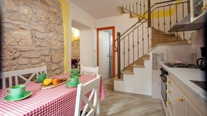 A kitchen with a stone wall, a staircase, and a table with a checkered tablecloth. - Pokrajac in Rovinjsko Selo  - Haus für 4-5 Personen (Rovinj)