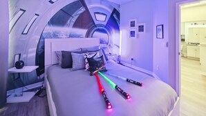 A modern bedroom with a curved ceiling, a bed with colorful lights, a bedside table, and a view of a bathroom. - Amazing Disney Themed Oasis 3br Near Parks 3 Bedroom Townhouse by RedAwning (Kissimmee)