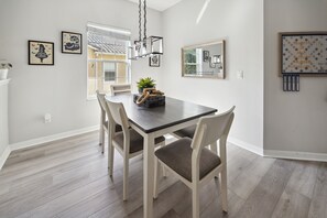 Un espace repas comprenant une table et des chaises en bois, un luminaire suspendu et des œuvres d’art murales.