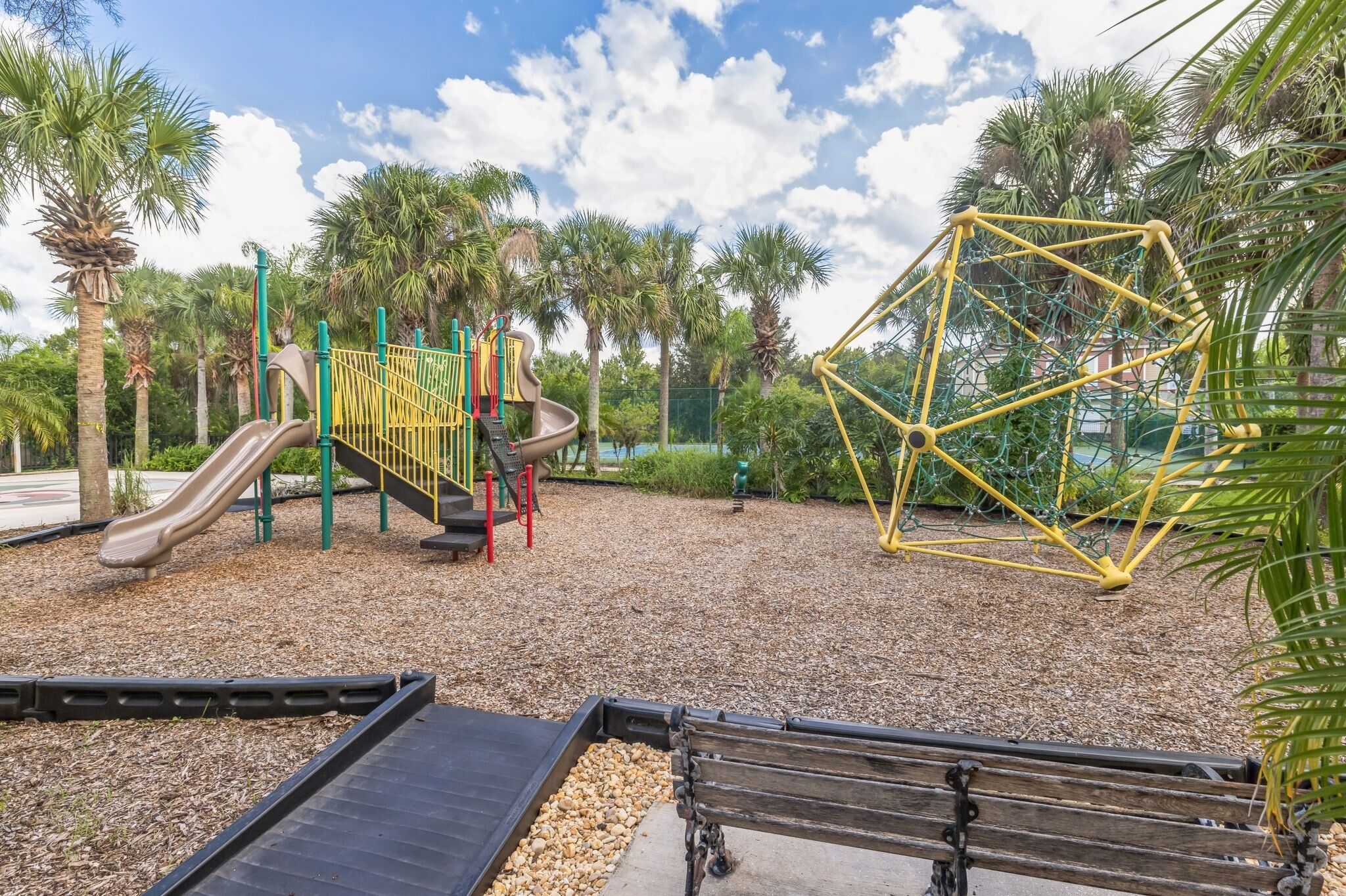 A playground with a slide, climbing structures, and a yellow climbing net.