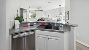 A modern kitchen with a stainless steel dishwasher, white cabinetry, and a grey countertop. - Amazing Disney Themed Oasis 3br Near Parks 3 Bedroom Townhouse by RedAwning (Kissimmee)