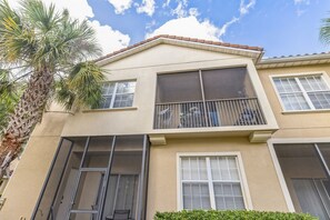 Un immeuble de deux étages, à la façade beige, doté de grandes fenêtres et d’un balcon avec des rampes en métal.