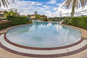 Une grande piscine circulaire, bordée de carreaux, entourée d’arbustes bien entretenus et de palmiers.