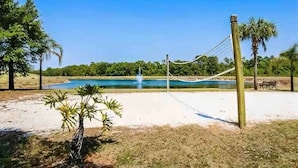 A volleyball net in a sandy area with a pond and trees in the background. - Amazing Disney Themed Oasis 3br Near Parks 3 Bedroom Townhouse by RedAwning (Kissimmee)
