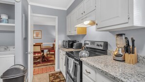 A compact kitchen with white cabinets, a granite countertop, a stove, a toaster, and a blender. - Centrally Located 4br Stonecrest Condo 4 Bedroom Condo by RedAwning (Lithonia)