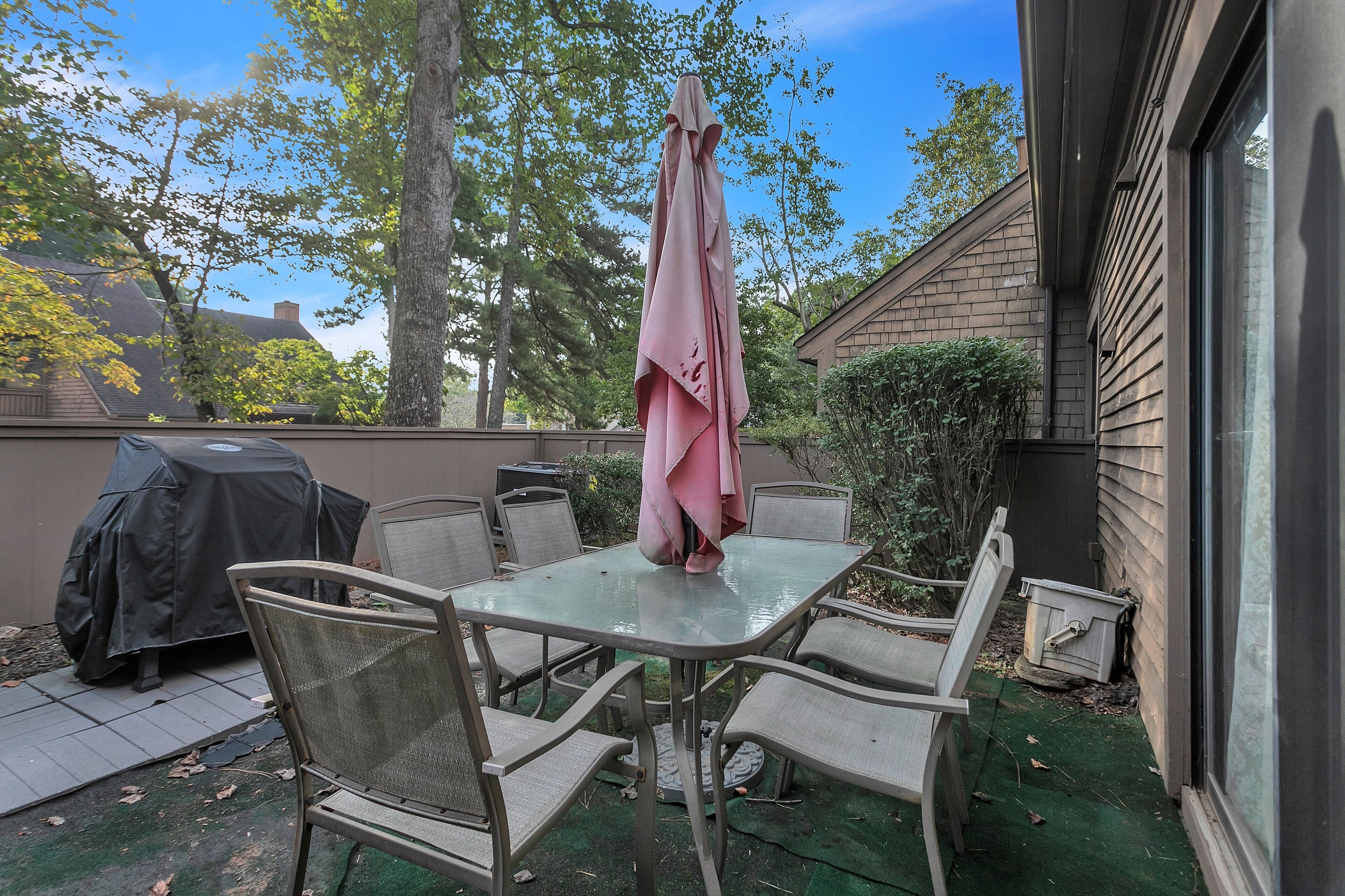 An outdoor patio with a table and chairs, a covered umbrella, and a grill.