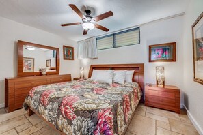 A bedroom with a wooden bed, a ceiling fan, a nightstand, and framed artwork on the walls. - Papakea #f108 1 Bedroom Condo by RedAwning (Lahaina)