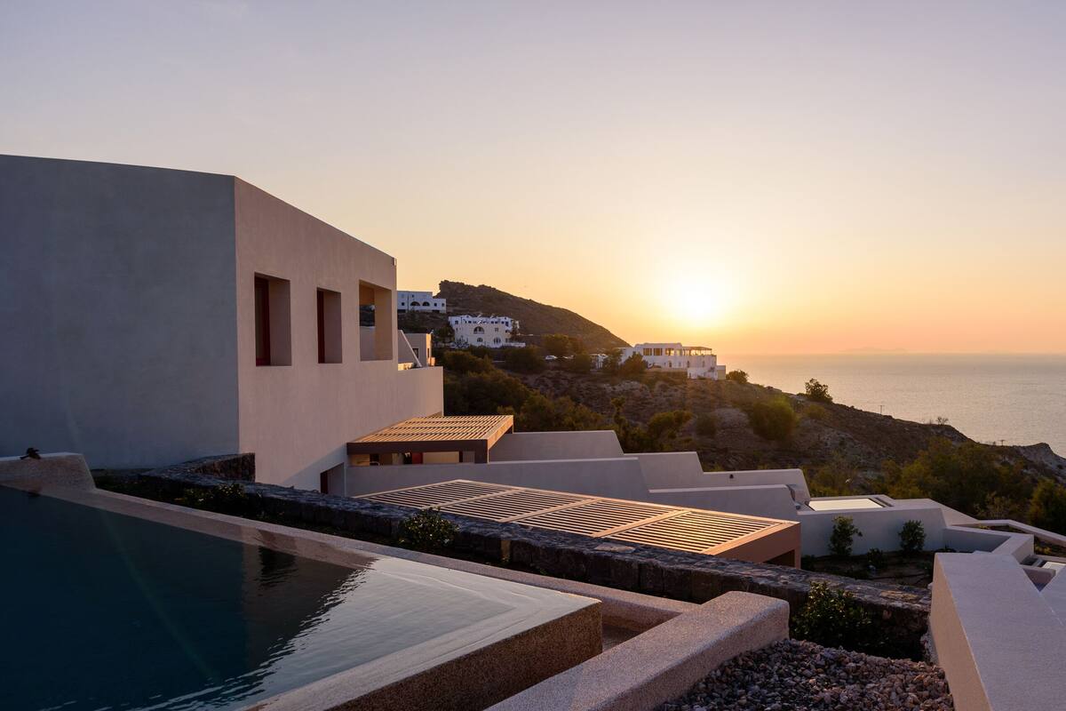 A modern building with a pool and a view of the sea at sunset.