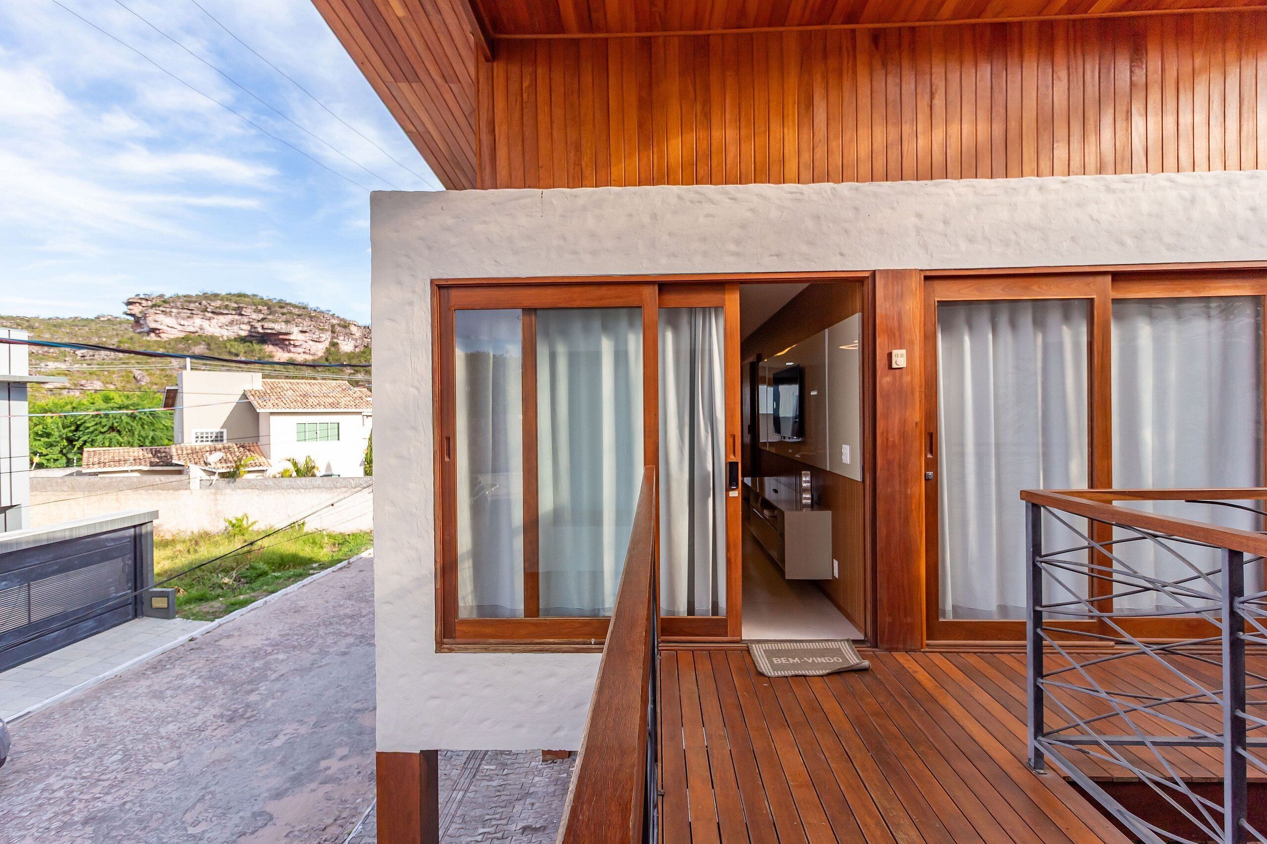 A modern house with a wooden deck, large sliding glass doors, and a view of a rocky hill.