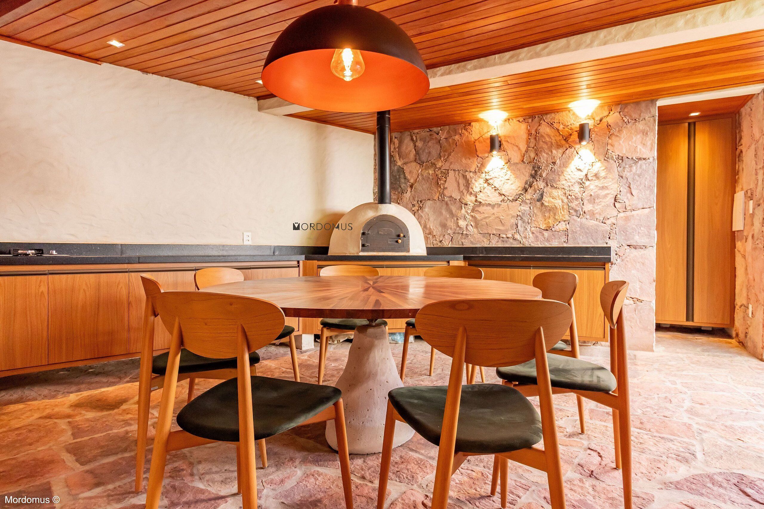 A modern kitchen with a stone wall, wooden ceiling, and a pizza oven.