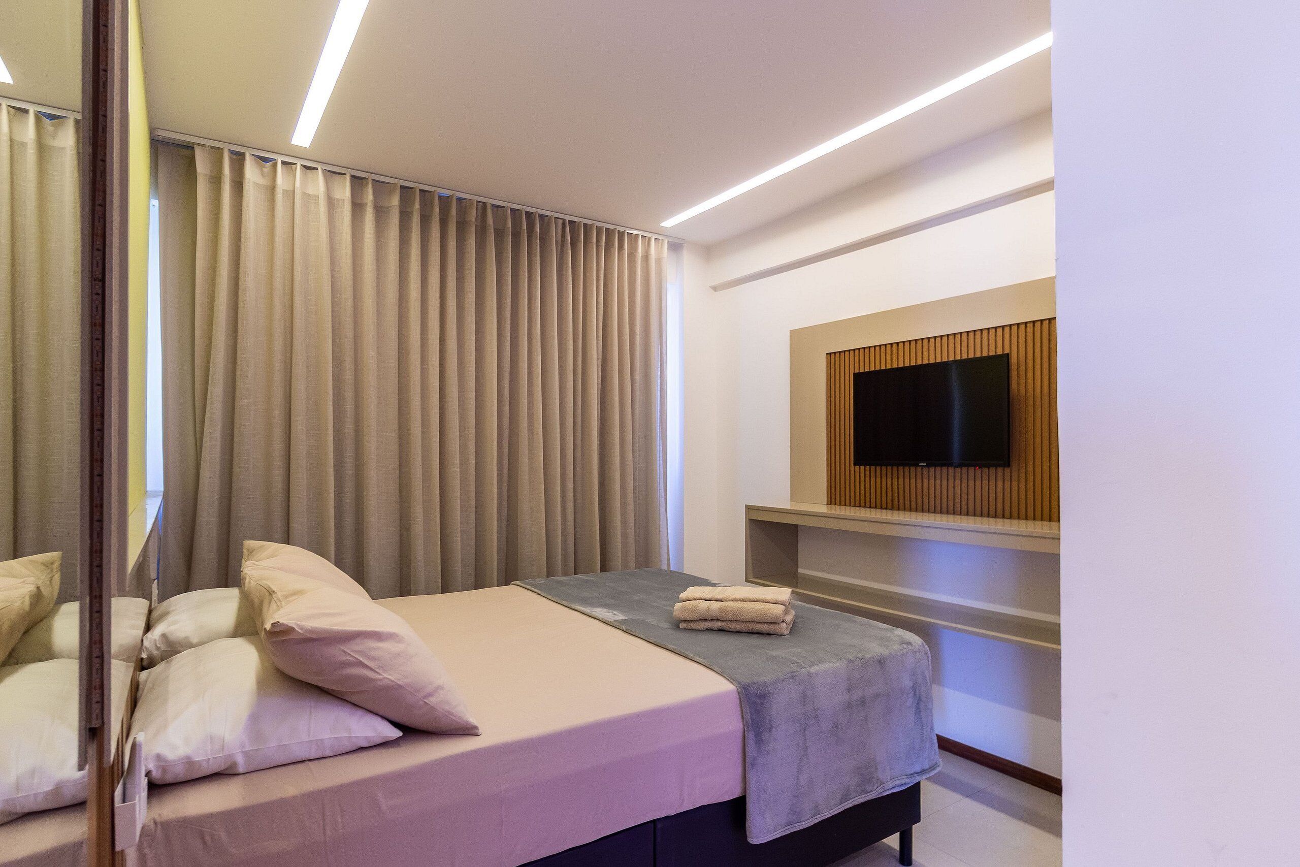 Una habitación de hotel moderna con una cama, un televisor de pantalla plana en la pared y un amplio ventanal con cortinas.