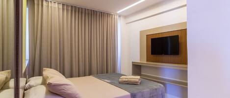 Una habitación de hotel moderna con una cama, un televisor de pantalla plana en la pared y un amplio ventanal con cortinas.