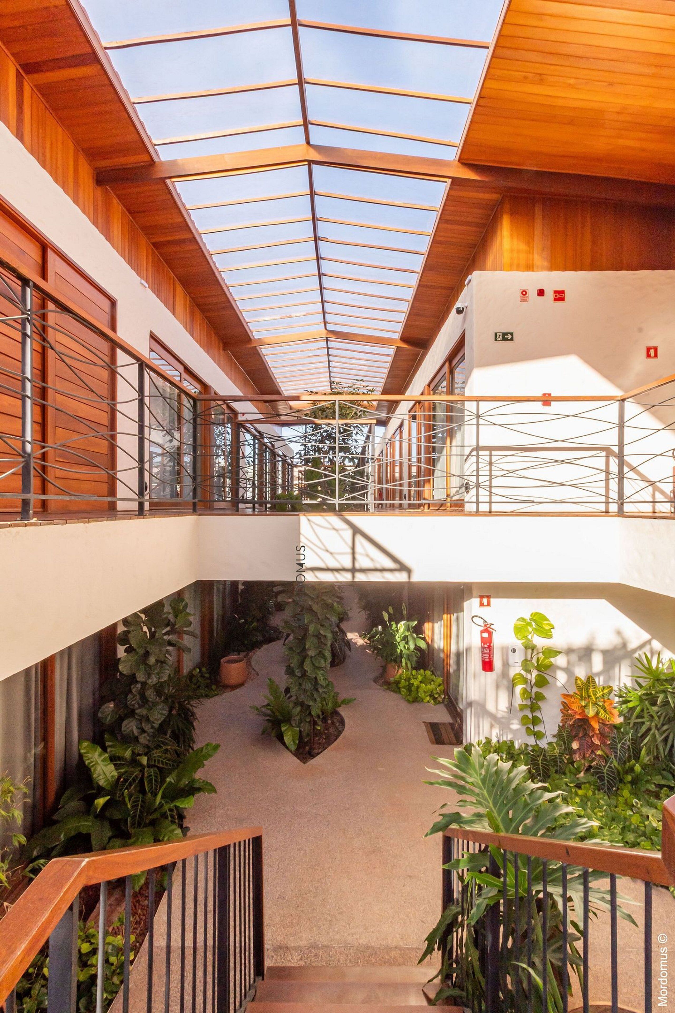 Ein modernes Interieur mit Glasdecke, Holzbalken und einer zentralen Treppe, die von Pflanzen umgeben ist.