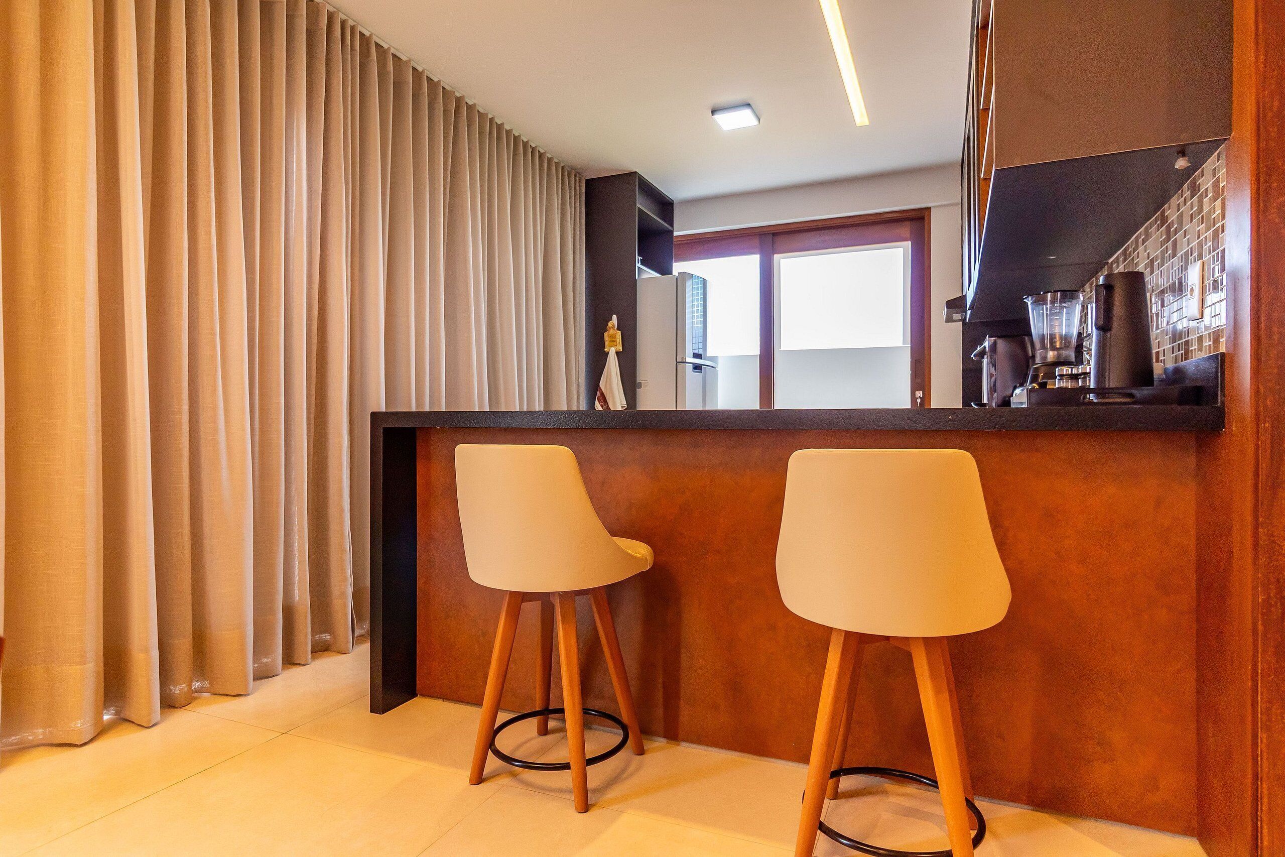 A modern bar area with two stools, a counter, and a view of the kitchen.