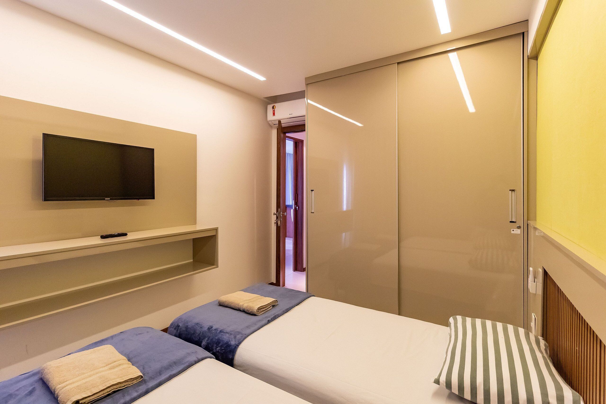 A hotel room with a flat-screen TV mounted on the wall, a sliding door closet, and two beds with towels and pillows.