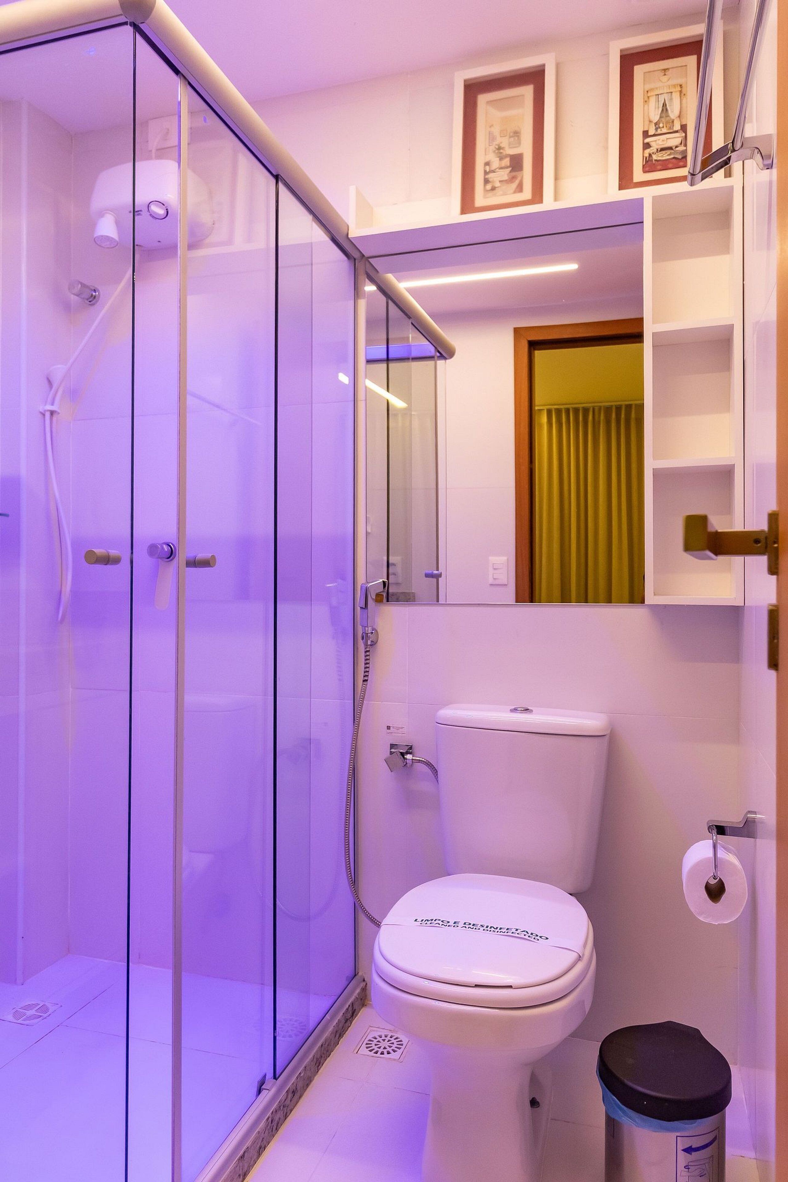 A bathroom with a glass-enclosed shower, a toilet, and a trash bin.