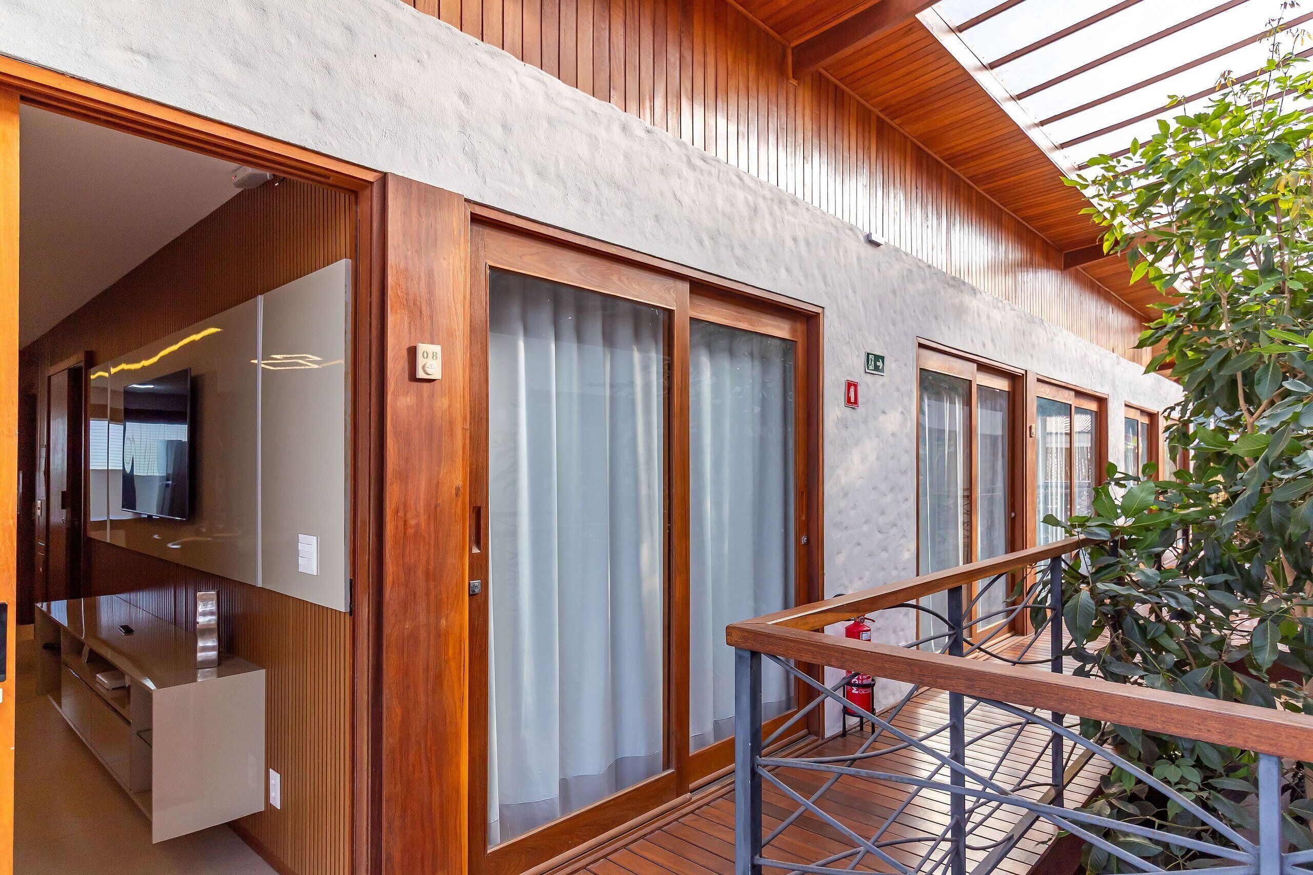 A modern hotel room with wooden paneling, large sliding glass doors, a wooden balcony, and a view of greenery.