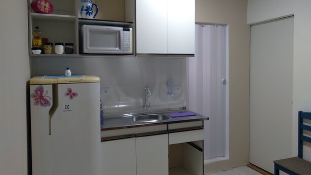 Una cocina compacta con microondas, lavamanos y un refrigerador pequeño.