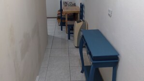 Un pasillo estrecho con una mesa y sillas azules, piso de baldosas y una puerta al final.