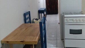 Una pequeña cocina con una mesa y sillas de madera, estufa y una puerta al fondo.