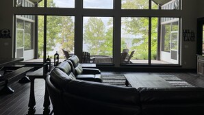 Un salon spacieux doté d’une grande fenêtre donnant sur un lac, d’une cheminée et d’un canapé en cuir.