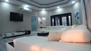 Una sala de estar moderna con un sofá blanco, un televisor de pantalla plana montado en la pared y un amplio ventanal con vistas al exterior.