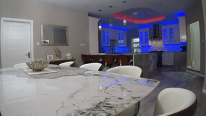 Una cocina moderna con iluminación azul debajo de los armarios, una isla de mármol y muebles blancos.