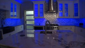 Una cocina moderna con una isla central, horno empotrado e iluminación azul.