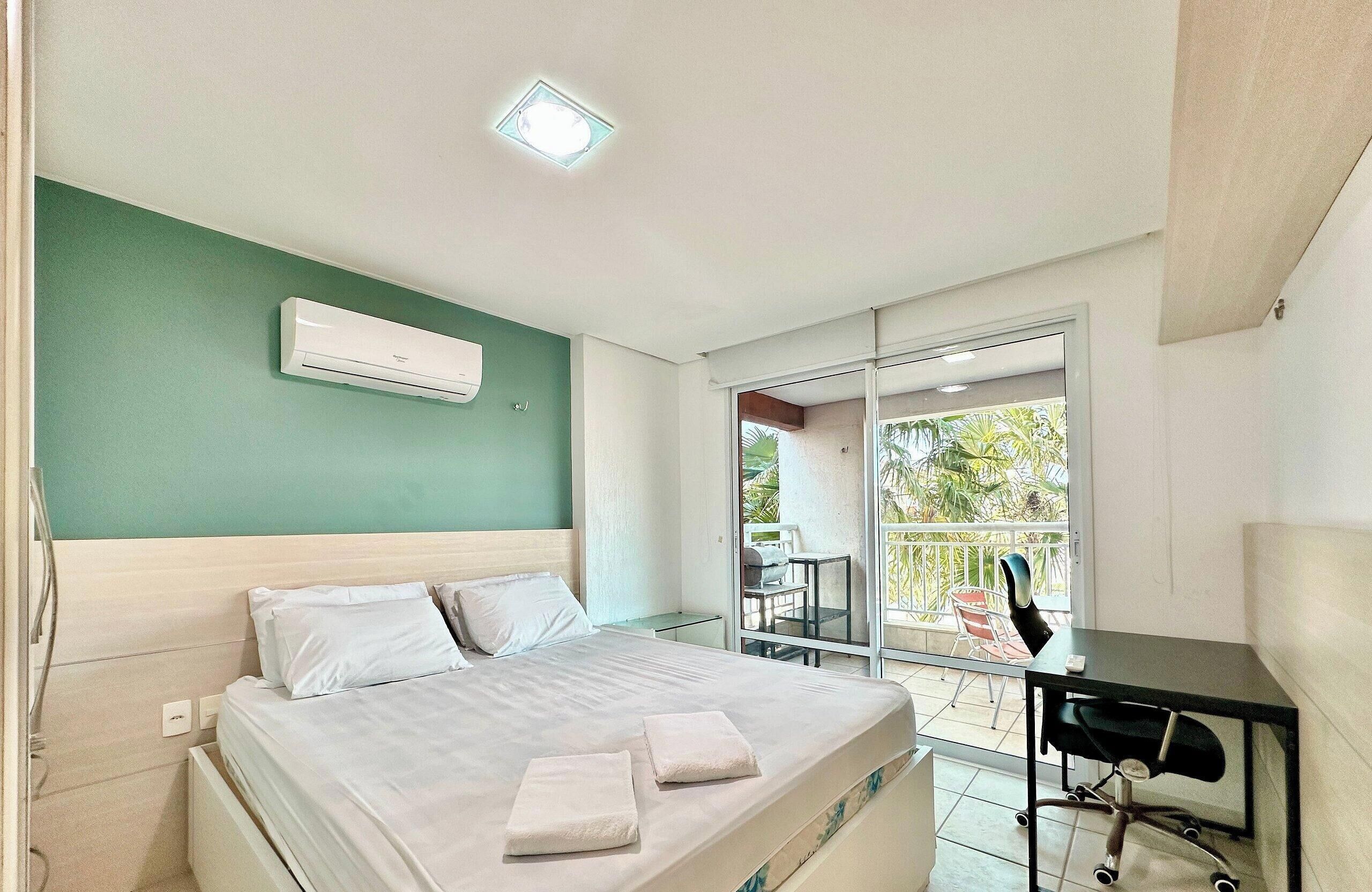 A hotel room with a bed, a desk, an air conditioner, and a balcony with outdoor furniture.